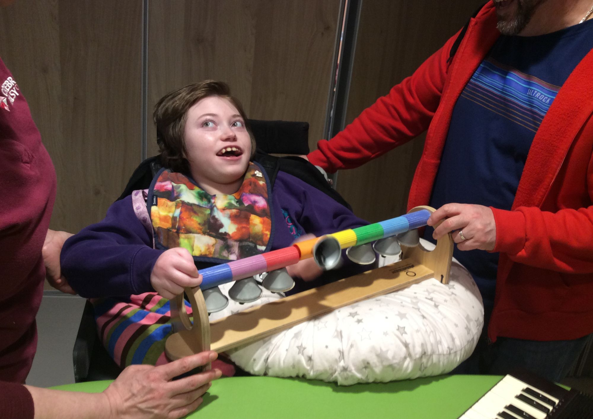 a teenager in a wheelchair playing with a musical instrument aided by a therapist